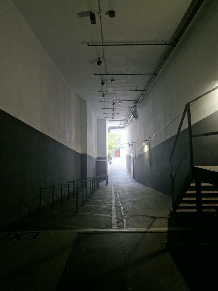 The covered passage behind the entrance, with a wide concrete floor sloping down towards the courtyard. Bicycle racks on the left, a metal staircase on the right beside the ramp.