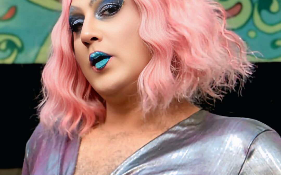 Miss Stray σε drag: ροζ περούκα, μπλε χείλη, ασημένιο τοπ.