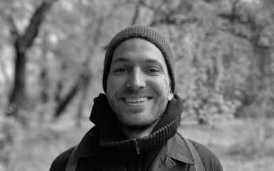 Christoph Heusmann χαμογελά, με σκούφο, σε δάσος.