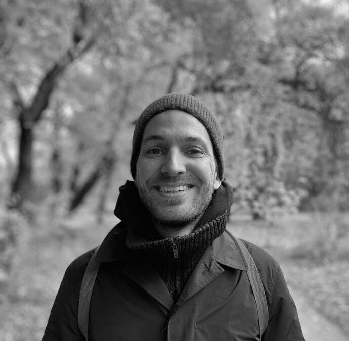 Christoph Heusmann smiling, in a wool hat, in a forest.