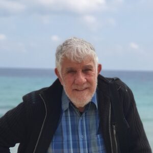 Γεώργιος Νεοφύτου χαμογελά, δίπλα στη θάλασσα.