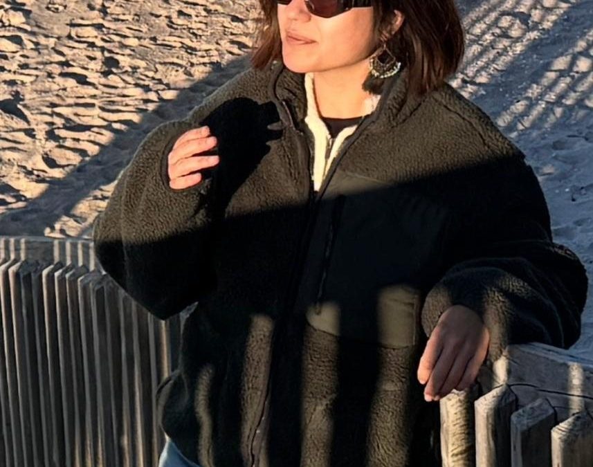 Irini Zorzos mit Sonnenbrille, an einem Zaun am Strand.